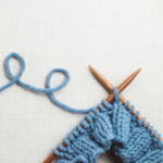 Wooden knitting needles with partially completed project using blue yarn.