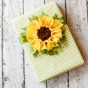 Present wrapped in green gingham print with a Sunflower bow on a distressed wood painted white background.