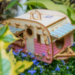 A handpainted miniature wooden camper fit for fairies set in a garden of blue blooms and green foliage.
