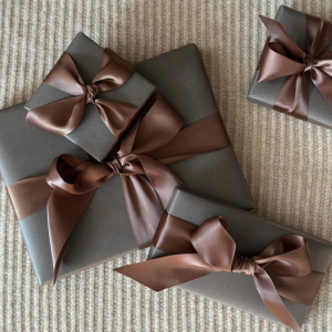 Presents wrapped in grey wrapping paper with brown satin bows scattered on a corduroy tableclothe.