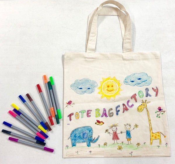 Paint pens laying on a white surface with a white canvas bag with children's drawings on it.