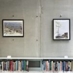 Two photographs of local Manitoba sites in black frames hanging against a cement wall above shelves of books.