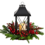 A black lantern with a Christmas wreath at it's base filled with a white candle.