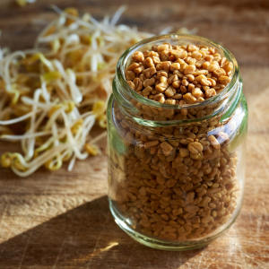 Seeds in a jar with sprouted seeds laying on a wood cutting board out of focus behind.