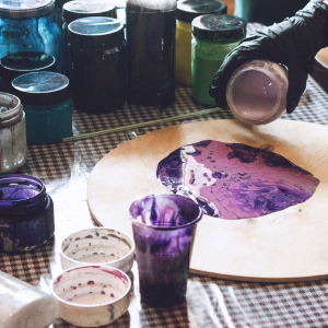 A jar filled with different hues of purple being poured onto a wooden circle atop a table.